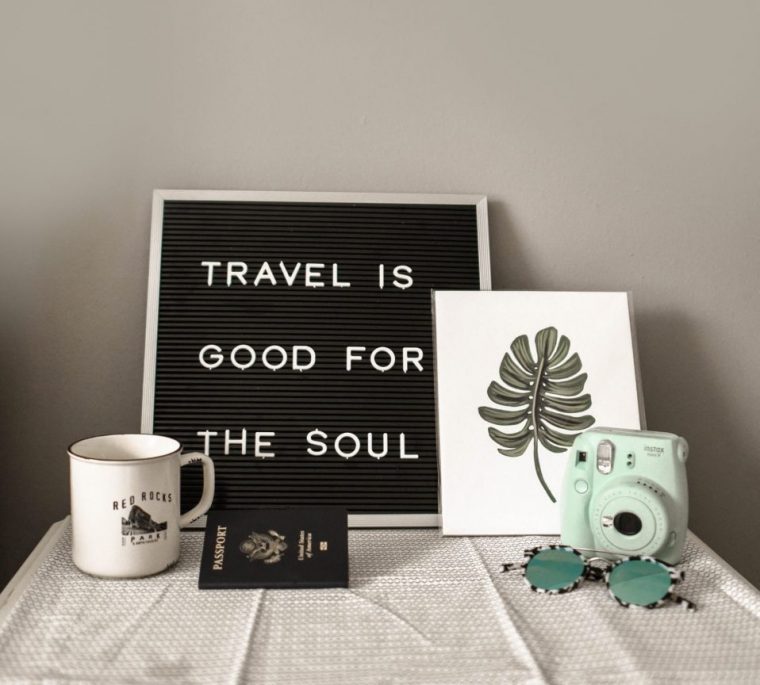 Travel quote on a black board with white letters, green camera and a passport