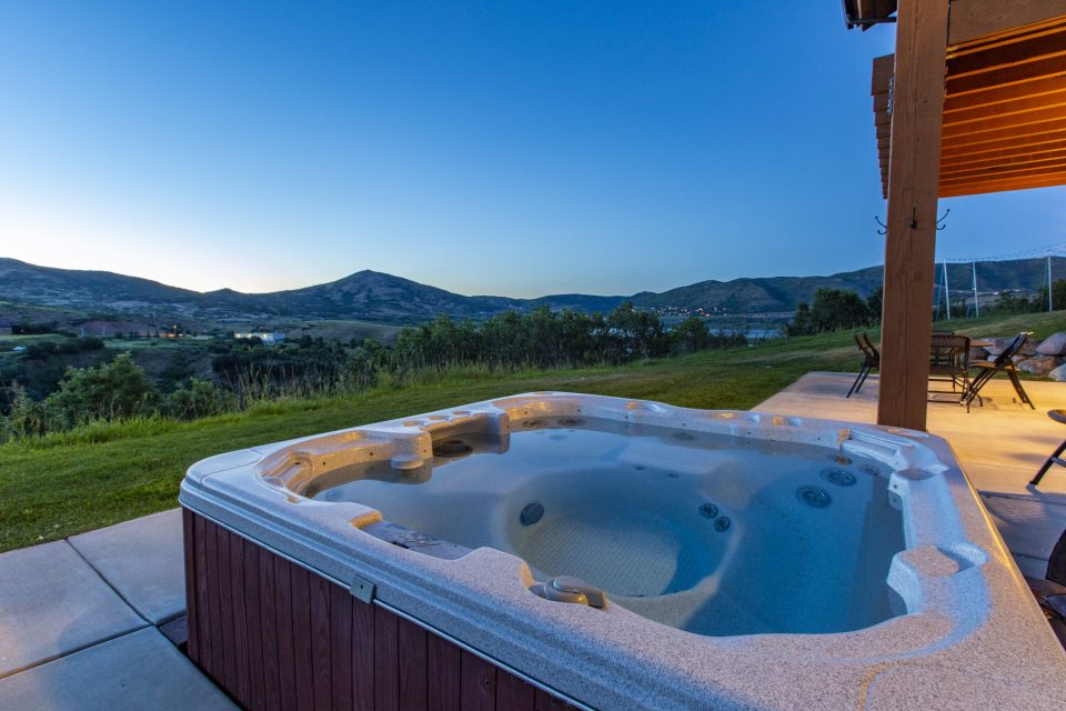 Hot tub overlooking green grass and the sun setting against the mountains.