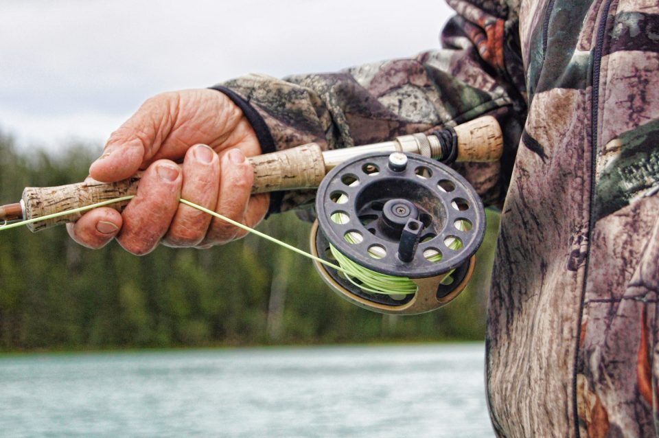 Up close of fishing pole with a person's hand holding the fishing pole. Used to show that fishing is a great summer activity. 