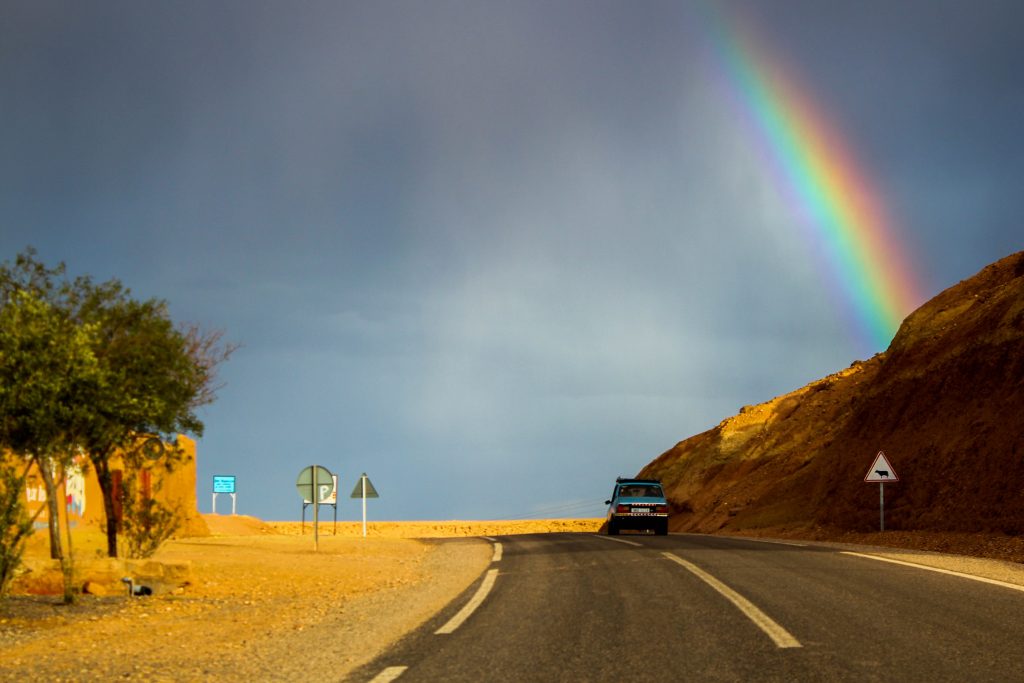 Car driving on an empty road with a rainbow over the road