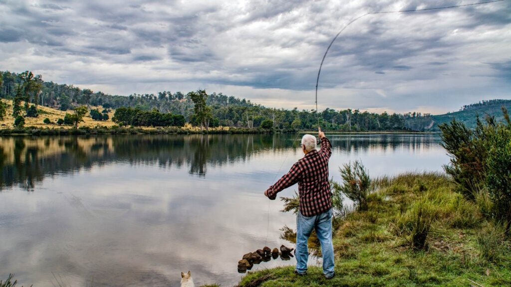 Man at lake fly fishing, still lake as he is about to cast his line 